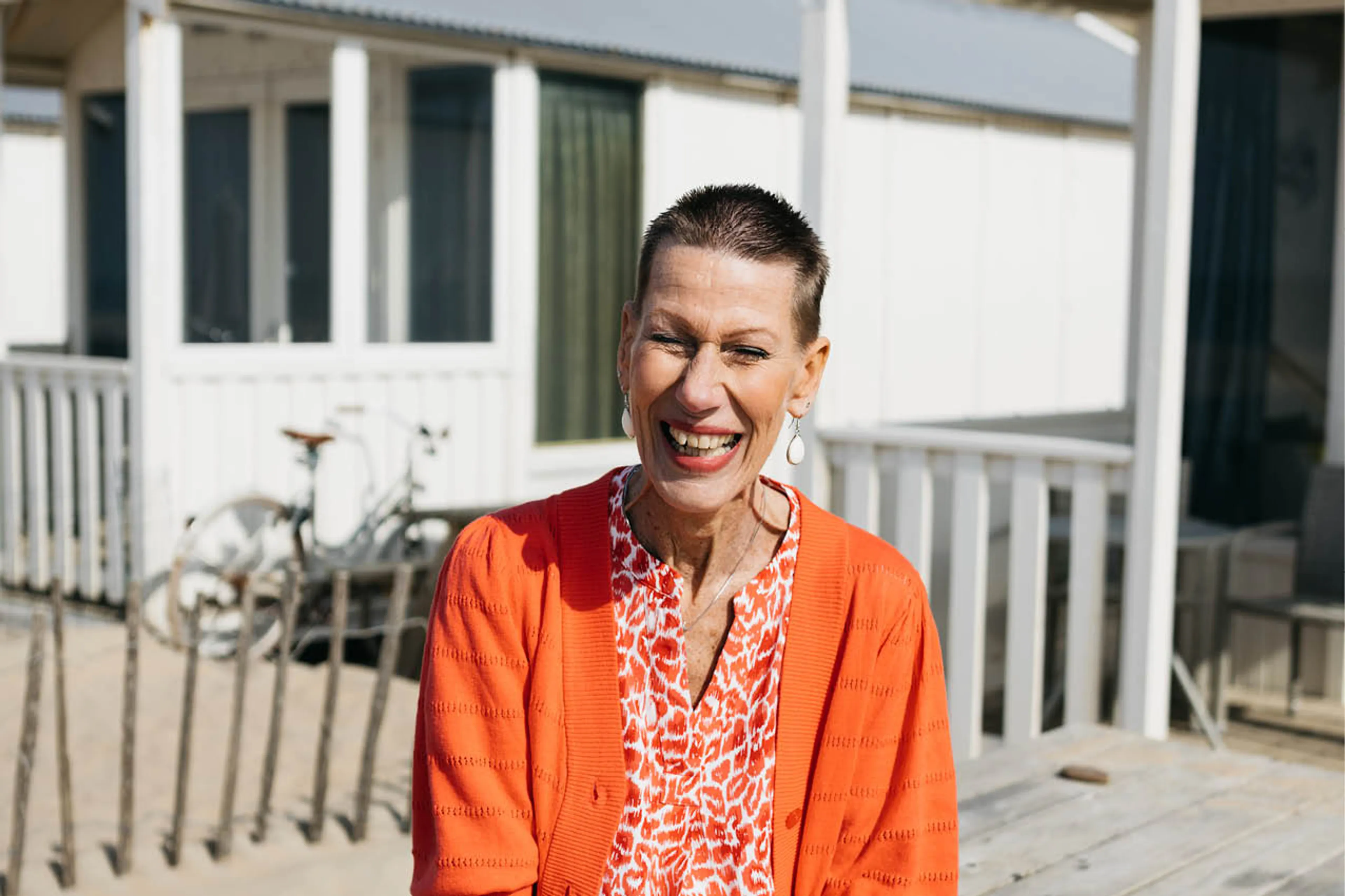 Ongeneeslijk zieke Marry is zorgmedewerker van het jaar. Ze zit op een veranda in de zon en lacht breeduit in de camera. Marry draagt een oranje vestje over een oranje met witte blouse. Onder haar korte bruine stekeltjeshaar draagt ze witte oorbellen.